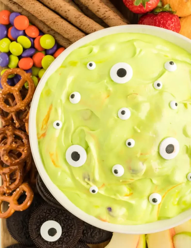 Green monster marshmallow dip topped with candy eyeballs, served with fruit for dipping