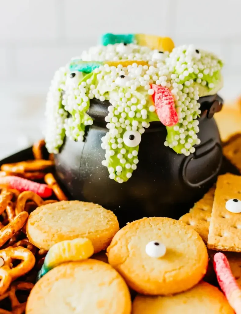 Green witches brew dessert dip overflowing from a black cauldron with gummy worms and candy eyes