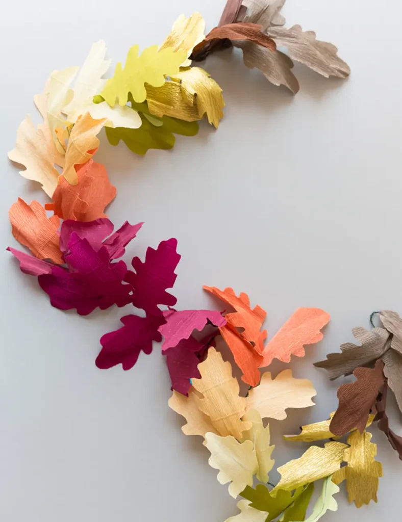 Handmade crepe paper leaf garland in brown, gold, orange and magenta shades hanging on a mantel
