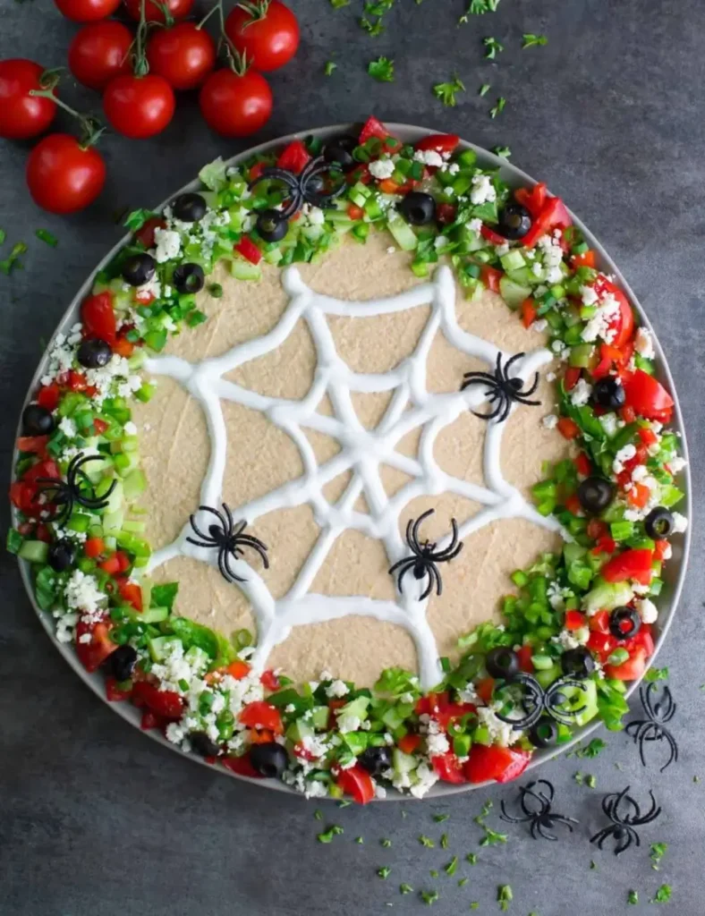 Hummus dip topped with a piped Greek yogurt spiderweb design and surrounded by chopped vegetable