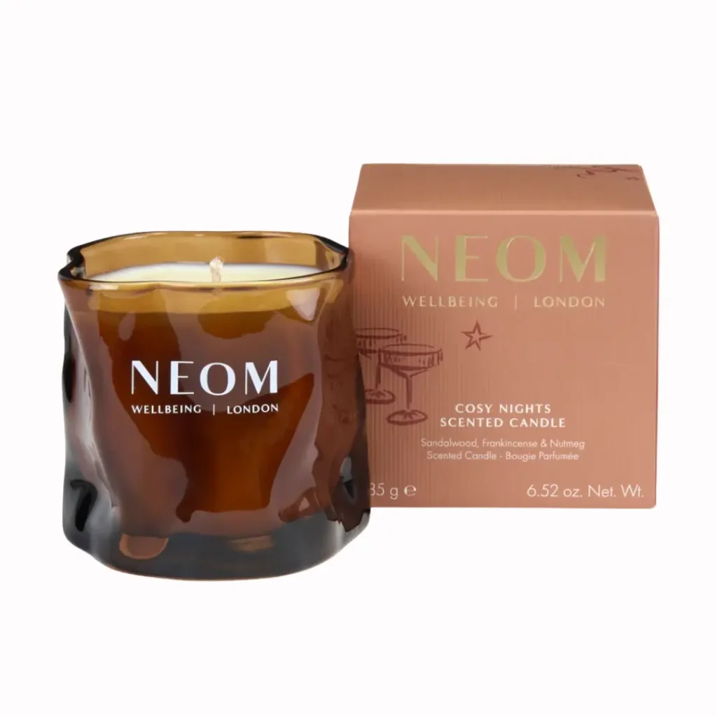 NEOM Cosy Nights scented candle in an amber glass jar beside its terracotta-pink gift box