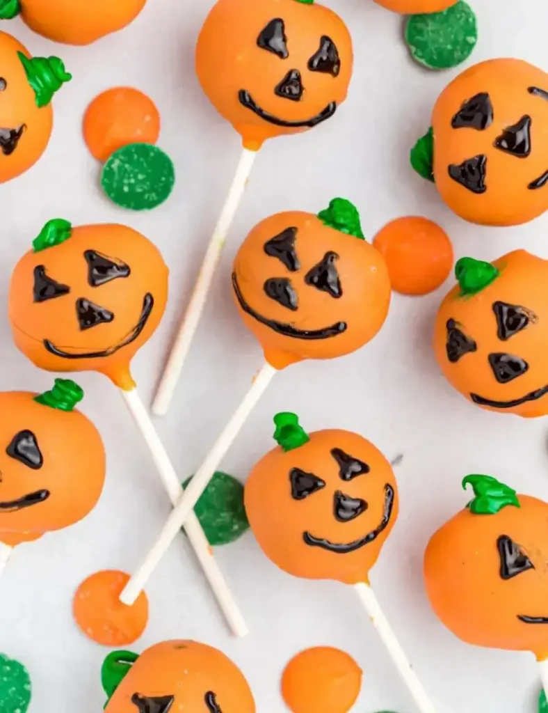 Orange jack-o'-lantern Halloween cake pops with green stems and black faces, displayed on a tray