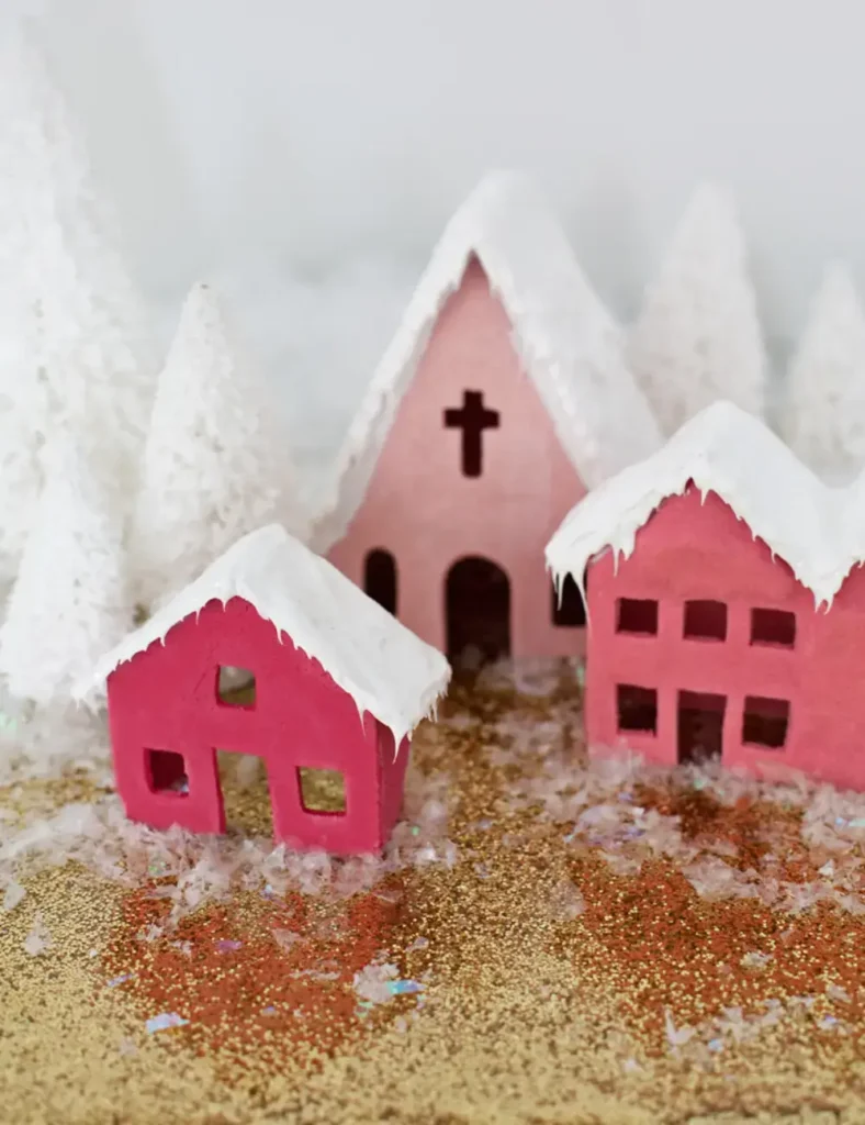 Pink salt dough village houses with glittery caulk roofs, glowing from battery tea lights inside, on a cabinet