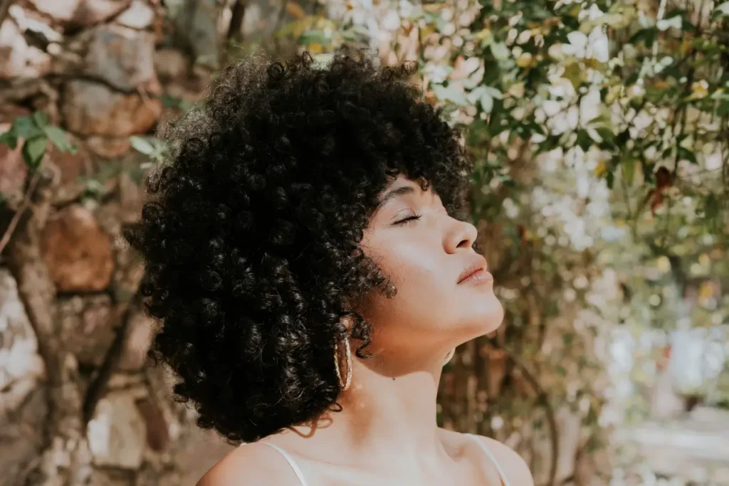 Portrait of a young woman with curly hair basking in sunlight outdoors.