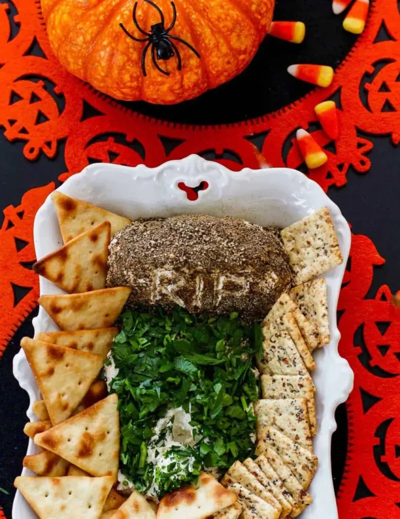 Savory cream cheese dip shaped into a tombstone with _RIP_ carved in and parsley grass alongside