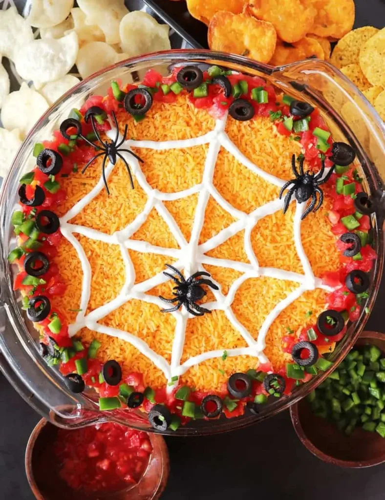 Seven-layer Halloween dip topped with a sour cream spiderweb design and plastic spiders