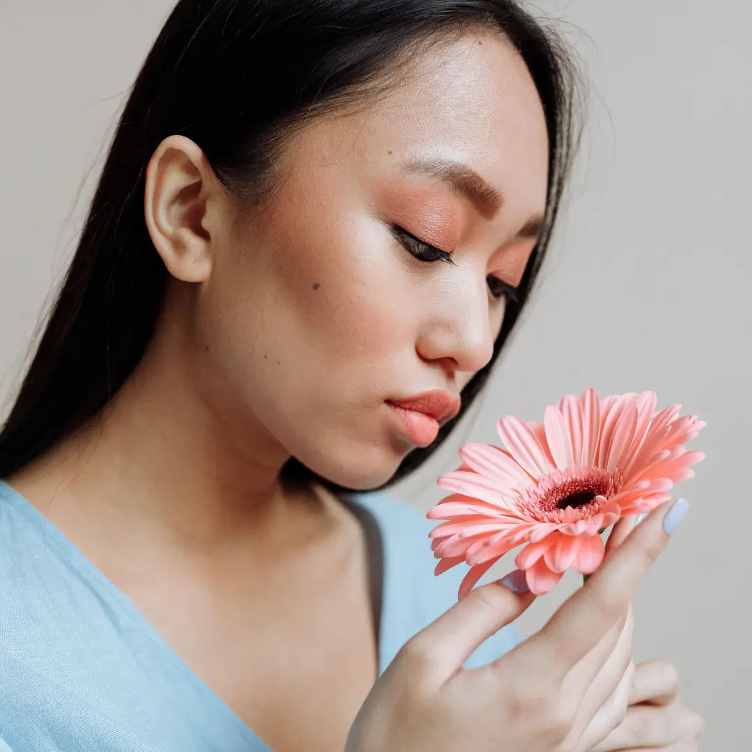 Side profile of an Asian woman admiring a pink gerbera daisy, creating a serene and elegant mood.