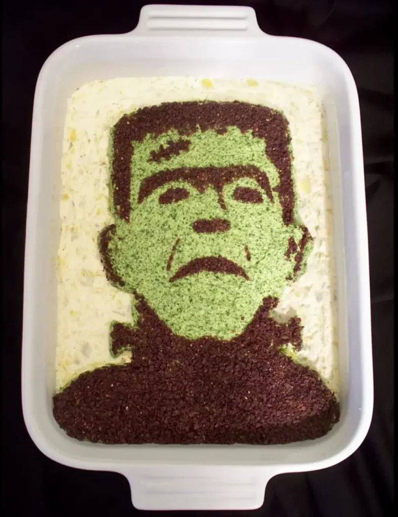 Spinach artichoke dip decorated to look like a green monster face using a stencil design