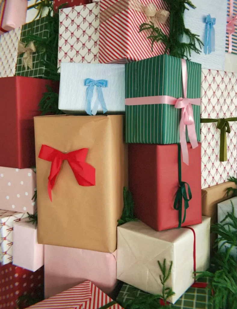 Stacked Christmas gifts in striped, polka dot, and kraft wrapping paper with colorful ribbon bows