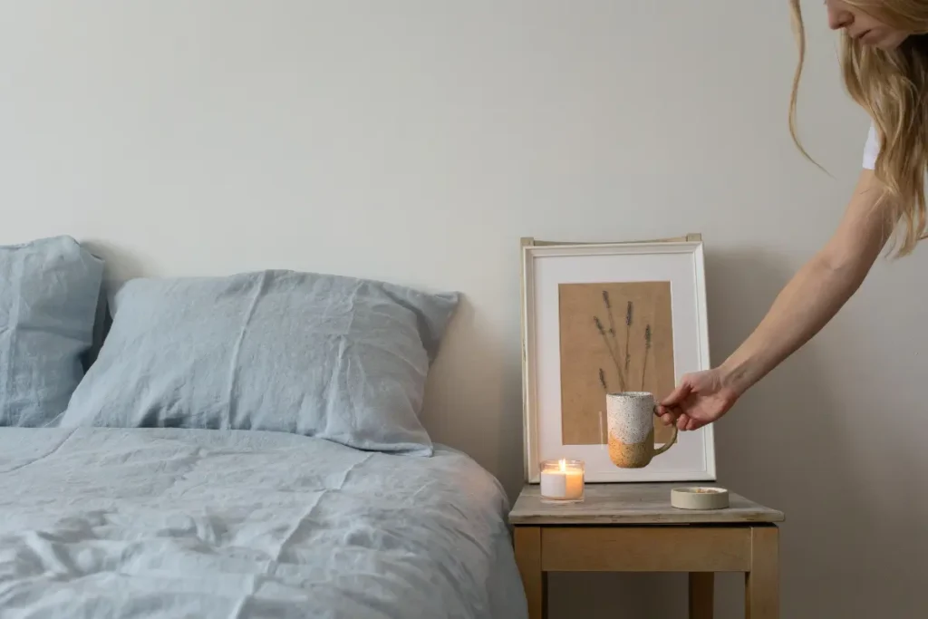 Stylish bedroom featuring a hand placing a coffee mug on a bedside table with a lit candle