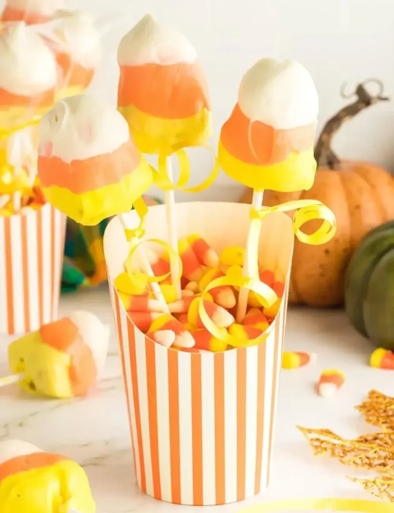Triangle-shaped candy corn cake pops in yellow, orange, and white, displayed in a striped cup
