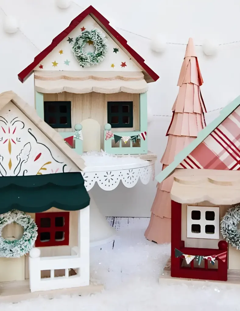 Unfinished wood Christmas village houses with patterned paper roofs, painted details and small bottle brush wreaths