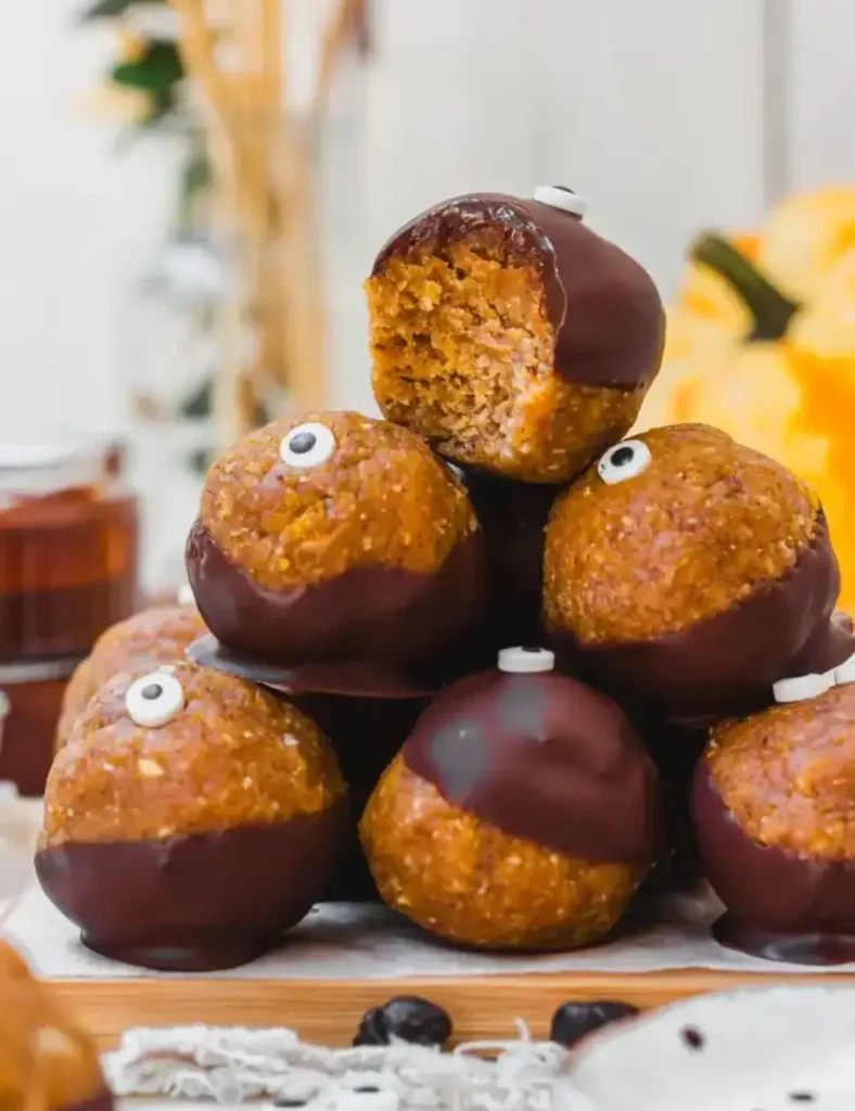 Vegan chocolate-covered pumpkin cake pop truffles with candy eyes, stacked on a plate
