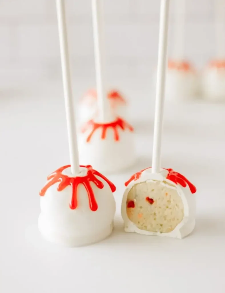 White Halloween cake pops with red _blood_ drips running down the sticks, arranged on a table