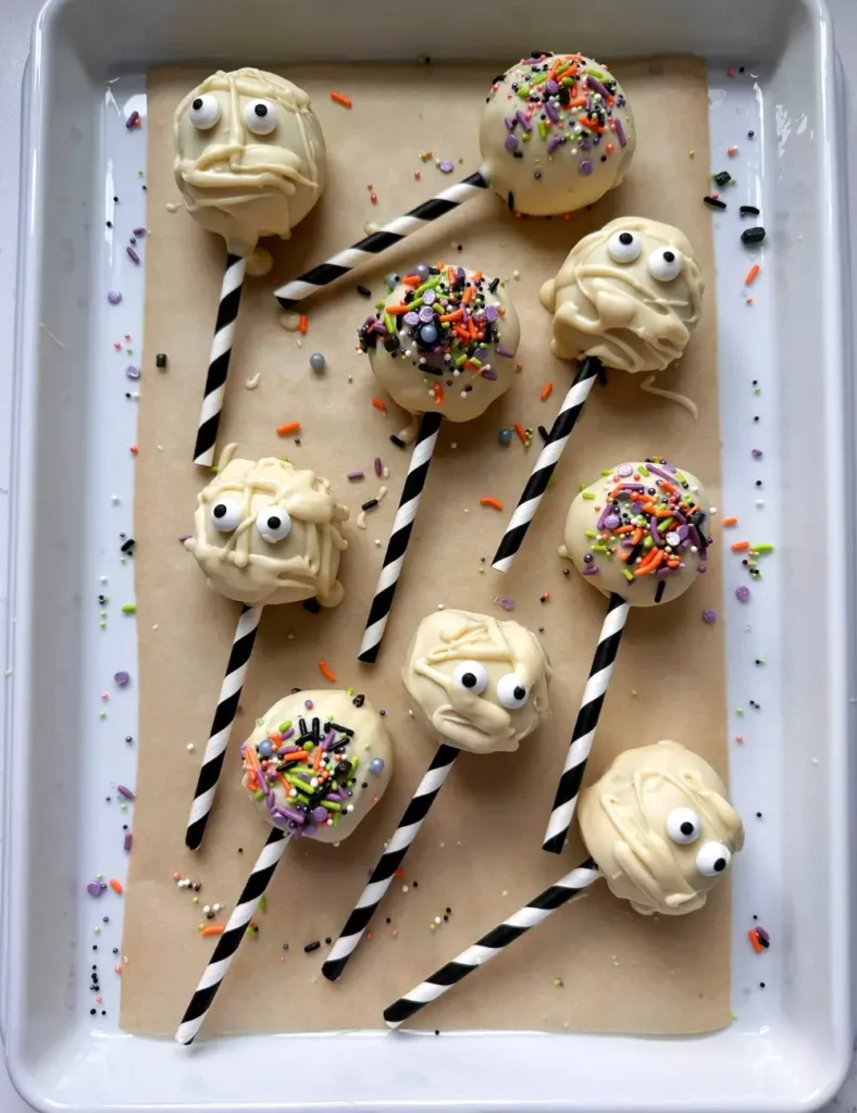 White chocolate mummy Halloween cake pops with candy eyes, arranged on a baking sheet