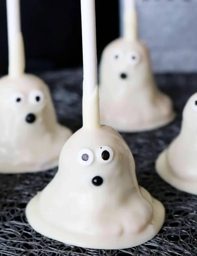 White ghost-shaped Halloween cake pops with candy eyes and black nonpareil mouths, standing upright