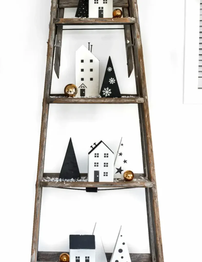 White painted wooden Christmas village houses with stenciled windows and doors and screw chimneys, displayed on a ladder shelf