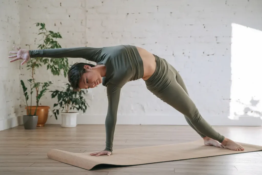 Woman in activewear performs a yoga pose on a mat in a bright indoor setting.