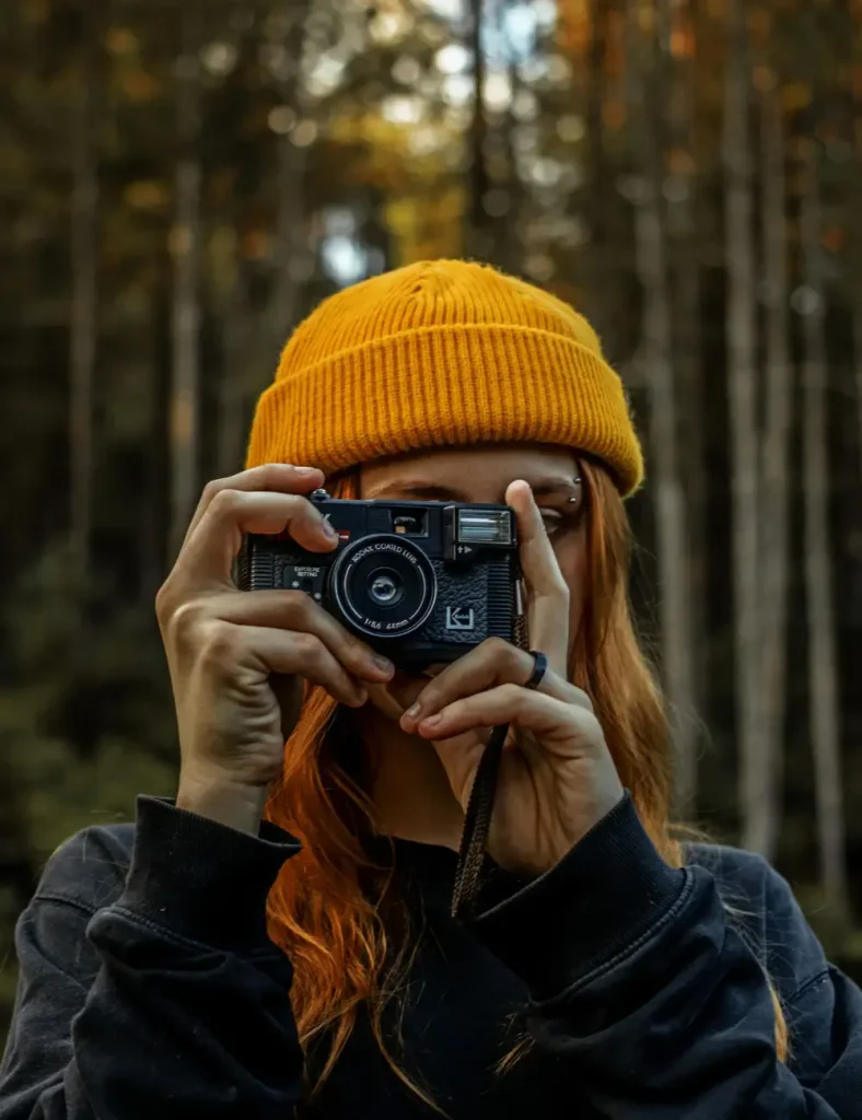 Woman holding vintage camera in forest setting, capturing nature's beauty
