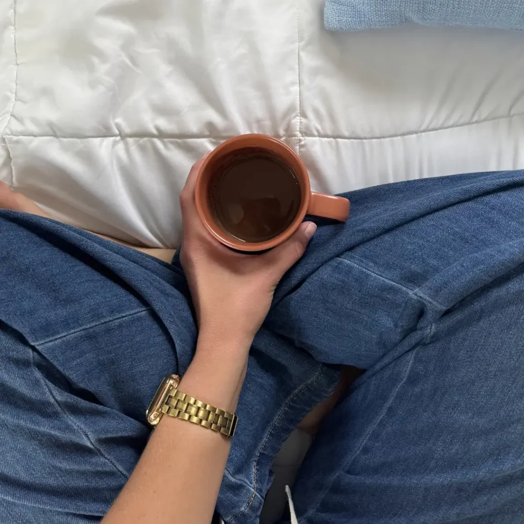 top view of a woman in jeans, sitting cross-legged holding a cup of coffee
